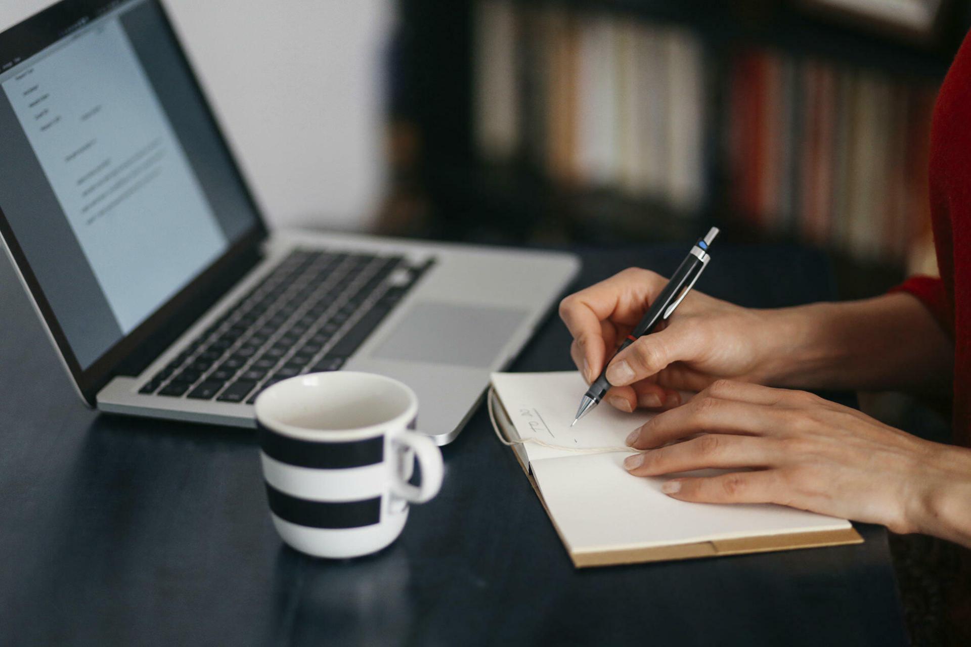Une personne devant un ordinateur qui écrit sur un papier